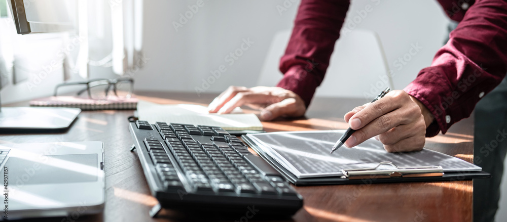 Poster Asian man programmer holding pen to writing code data on document in clipboard while working to recheck code