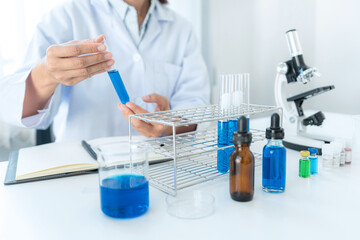 Fototapeta premium Scientist woman holding test tube in his hands and checking blue liquid from test tube while working