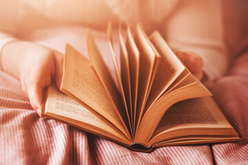 A man in a white sweater is lying on a bed with a pink striped blanket and flipping through the pages of an old interesting book. Self-development. Recreation and pastime.