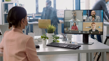 Executive businesswoman with medical face mask having online videocall meeting with remotely team during coronavirus pandemic. Team respecting social distance to prevent infection with covid19