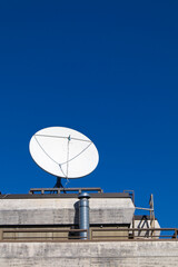 White satellite dish antenna on the roof against blue sky