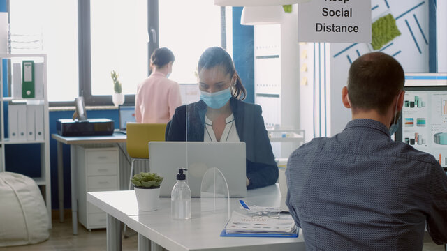 Business team with face masks working in company office taking precaution to mantain safety measures to avoid coronavirus infection. Collegues respecting social distancing during covid19 quarantine - Powered by Adobe