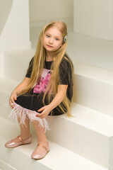 Cute little girl is sitting in the studio on the white stairs. style and fashion concept, happy childhood.