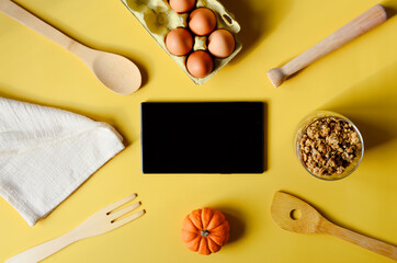 Flat lay with tablet with black mockup and place for text on yellow background. Food blogger's workplace. Culinary blog, recipe template, online cooking courses. Healthy food concept. Copy space.