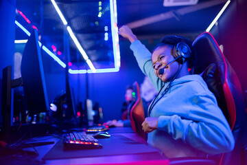 Young african happy woman professional gamer win in online video game with headphones, neon background