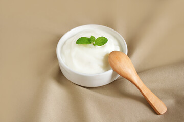 Yogurt natural flavor in white ceramic bowl with peppermint leaf and wooden spoon placed on light brown cloth, Milk curd organic homemade or Processed dairy products for Health care and Healthy food.