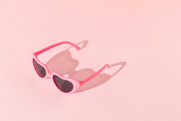Pink sunglasses with sunlight shadow on pastel pink background. Minimal summer love concept.