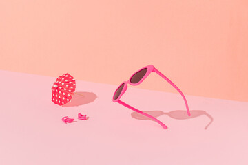 Pink sunglasses, heels and sun umbrella with sunny day shadows against bright pink and peach color background. Minimal summer beach fun concept. © Boba