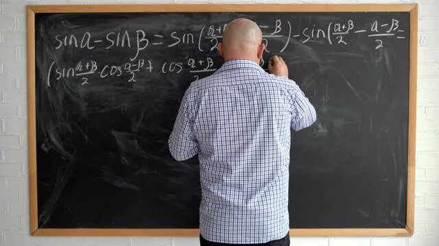 The teacher at the blackboard is a man of 40s without a face, writing down mathematical formulas with chalk. Online math lesson.