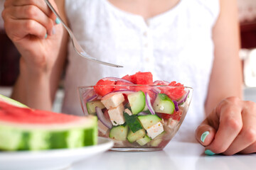 Young woman eats fresh dietary salad with watermelon and feta cheese for breakfast. Healthy food concept. Close-up.