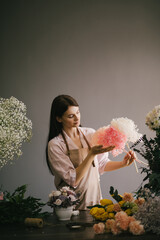 Young woman florist working in her flower studio, making beautiful bouquet using fresh plants and flowers. - obrazy, fototapety, plakaty