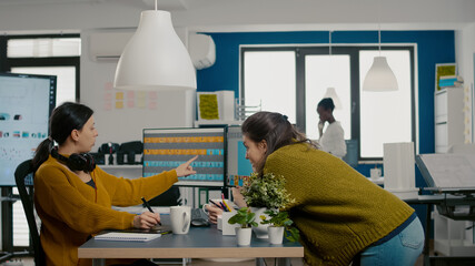 Graphic designers analysing client assets from displays checking color greading and taking notes. Retouchers working in photo editing software app holding stylus pen sitting in creative acgency office