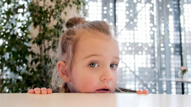 Thoughtful blonde little girl with pigtail leans on counter