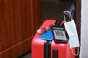 New normal concept. Close up view of a smartphone with an immune digital health passport, a red suitcase, protective mask, passport and sunglasses. Traveling by plane during a pandemic.