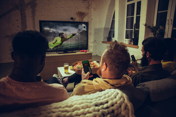 Group of friends watching TV, sport match together. Emotional fans cheering for favourite team, watching on exciting game.