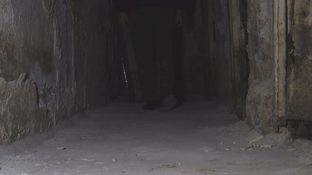 Man walking down the dark corridor of an old abandoned basement. Front view. Low key
