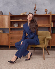 Young beautiful woman in blue blazer and pants sitting at green armchair in bright stylish...