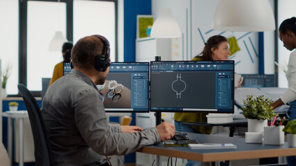Engineer with headset working on PC, screen showing CAD software with 3D construction metalic...