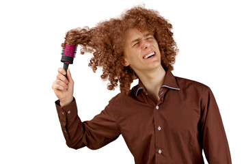 A long-haired curly-haired guy in a brown shirt on a white background uses a metal round comb. Emotions before a haircut in a hairdresser. Pain from combing