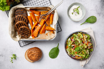 Grilled meat free plant based cutlets with sweet potato wedges, green mix salad and white sauce on...