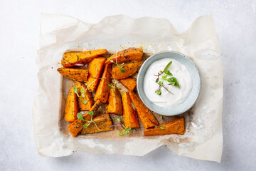 Sweet potato wedges. Oven baked sweet potato with herbs served with  white sauce on gray background. Healthy vegetarian food concept. Top view.