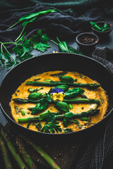 Omelette with green asparagus, basil and herbs on black background, vertical