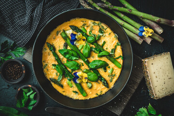 Omelette with green asparagus, basil and herbs on black background, top view