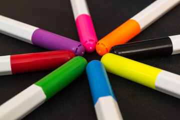 Multicolored markers in the shape of a star on a black background. Center close-up.