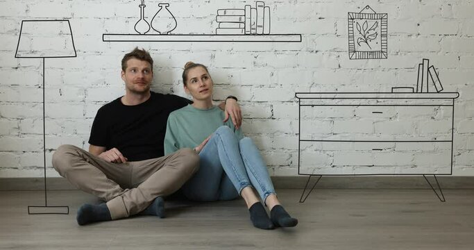 happy couple sitting on floor in new house and planning new home interior. furniture sketch