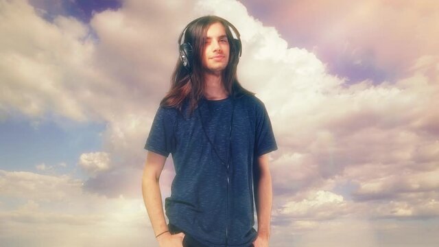 Dreamy Music Headphones Listen Happy Teenager. Young man with long hair enjoys music on his headphones on Heavenly background.