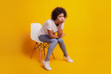 Beautiful unhappy girl sit chair fist cheek grumpy look isolated on yellow background