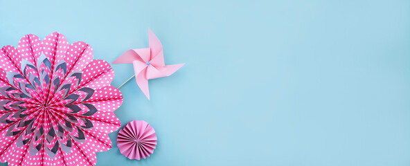 Fototapeta na wymiar Pink flower made of paper and paper windmill on light blue background. Banner image with copy space 