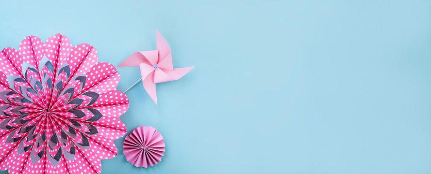 Pink flower made of paper and paper windmill on light blue background. Banner image with copy space 