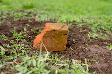 Red-yellow brick presses the covering material of the greenhouse (spanbond) and lies on a green lawn