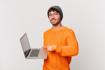 nerd man with computer smiling cheerfully, feeling happy and pointing to the side and upwards, showing object in copy space