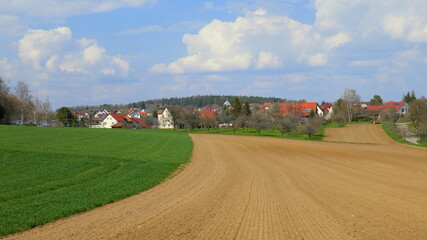 Fototapeta na wymiar idyllisches Dorf Mindersbach zwischen Feld und Wiesen unter schönem Wolkenhimmel im Frühling