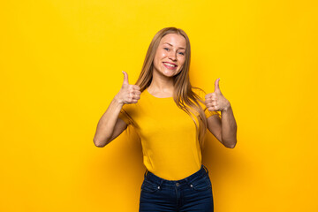 Happy brunette woman showing thumbs up and looking at the camera over yellow background