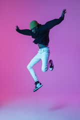 Fototapeta na wymiar Young stylish man in modern street style outfit isolated on gradient background in neon light. African-american fashionable model in look book, musician performing.