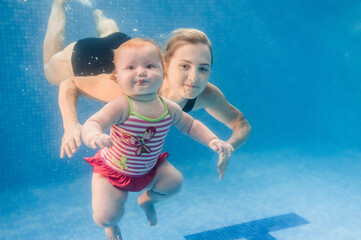 Mother holds baby, daughter learn to swim on swimming lesson, doing physical exercises, dive underwater with in pool. Healthy lifestyle, active parents. Enjoy of swimming and bubbles.