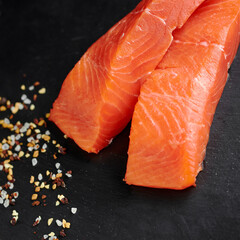 two pieces of fresh salmon fillet on a black background and pepper