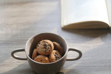 Bowl of chocolate chip cookies and open book on a table. Selective focus.
