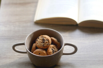 Bowl of chocolate chip cookies and open book on a table. Selective focus.