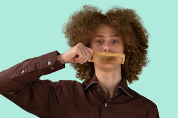 A long-haired curly-haired guy in a brown shirt on a blue background uses a wooden comb. Emotions...