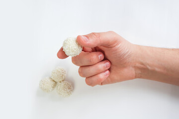Male hand holds white chocolate candy on white background. Handmade candies, Sweet balls. Isolated background. Selective focus.
