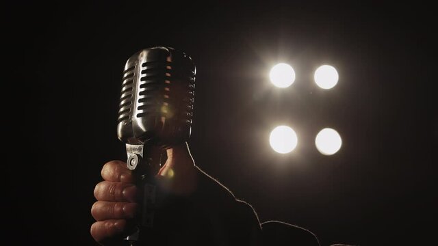 The singer is taking a retro microphone with his hand. The spotlight is shining on him. Close-up shooting. 4K