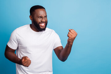 Fototapeta premium Portrait of positive crazy man raise fists celebrate win over blue background