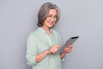 Portrait of attractive cheerful gray-haired woman using e-book reading searching isolated over grey pastel color background