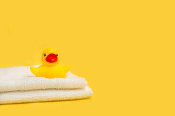 Pato de goma amarillo sobre unas toallas blancas sobre un fondo amarillo liso y aislado. Vista de frente. Copy space © Mercedes Fittipaldi