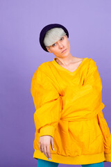 Stylish european woman on purple  background posing wearing yellow large jacket and hat