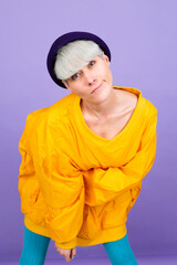 Stylish european woman on purple  background posing wearing yellow large jacket and hat